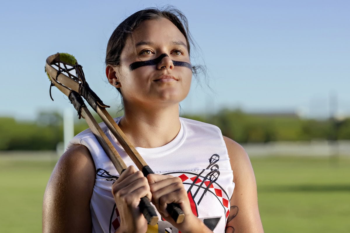 Kyra Dewayne Hornbuckle poses in a field with stickball sticks