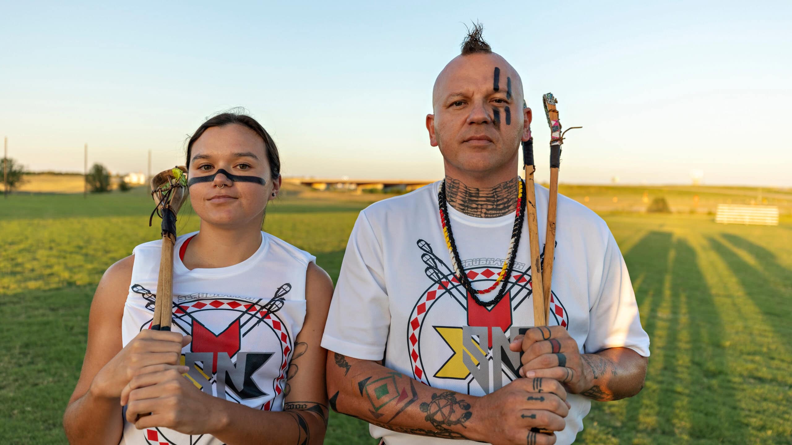 Dwayne and Kyra Hornbuckle pose in a field with their stickball sticks