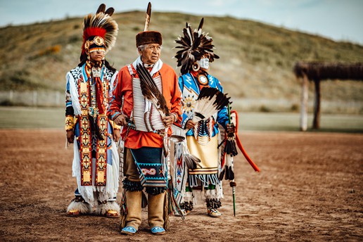 Wilson Roberts and two others stand in front of a mound in traditional Choctaw dress