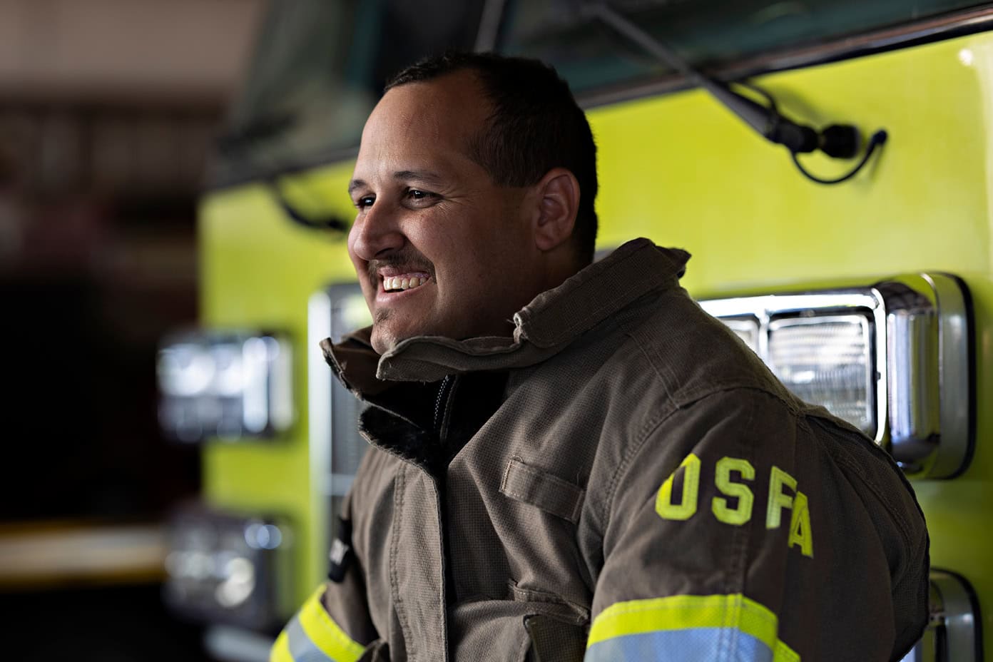 Jake Trujillo smiles on the front bumper of a fire truck