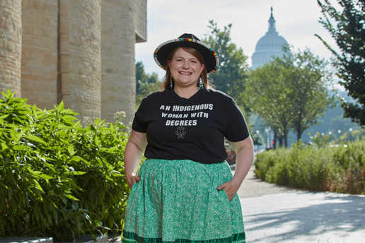 Kelbie wears a black hat and a black shirt reading "An indigenous woman with degrees"