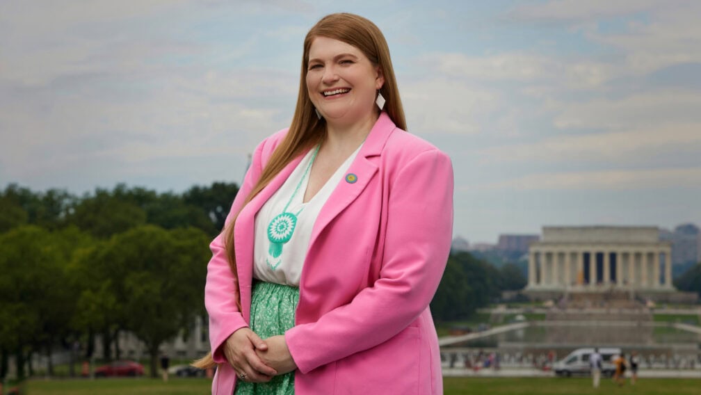 Kelbie Kennedy stands in front of the Lincoln Memorial in Washington D.C. in a bright pink suit with Choctaw jewelry and accent pieces.