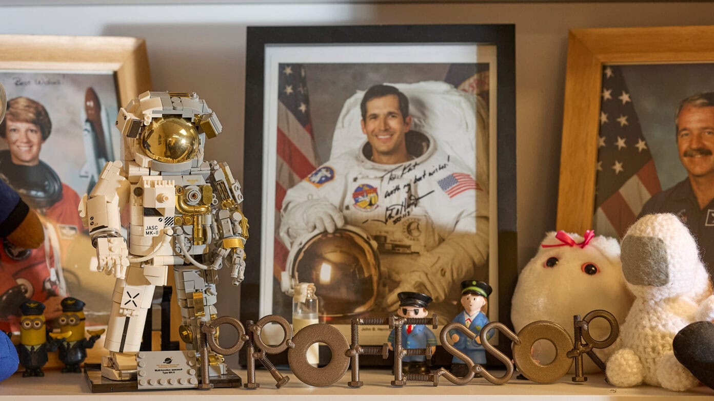 Lego astronaut figure among framed photos of space missions and plush toys, highlighting space exploration and honoring astronauts.