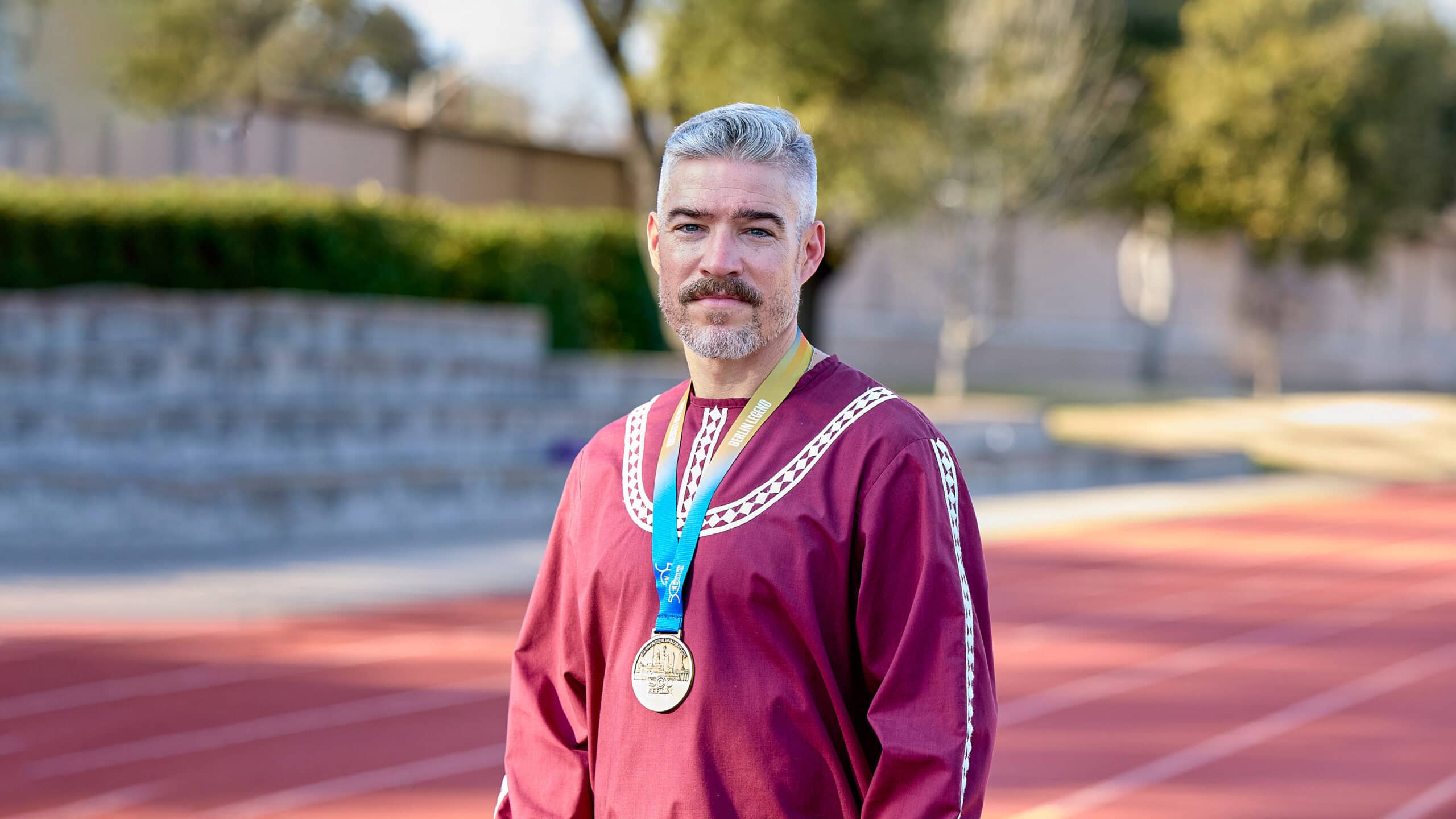 Corey Berlin wearing his choctaw shirt with a medallion while on a track field
