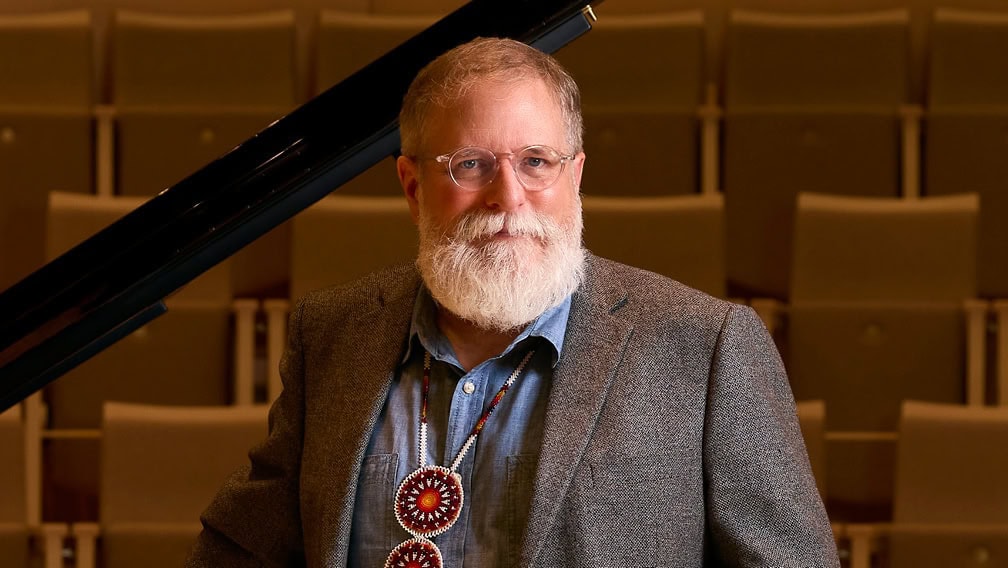 Profile view of Charles Shadle standing in front of piano